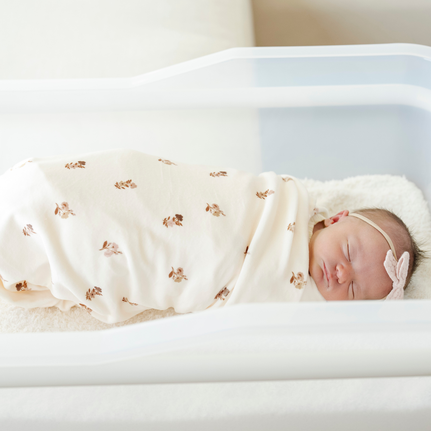 A newborn baby girl is swaddled in a floral blanket that is a minky stretch luxe swaddle.