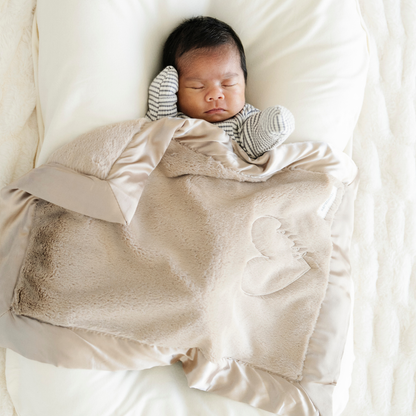 Baby boy snuggled in Satin Border Mini baby blanket in Tan. 