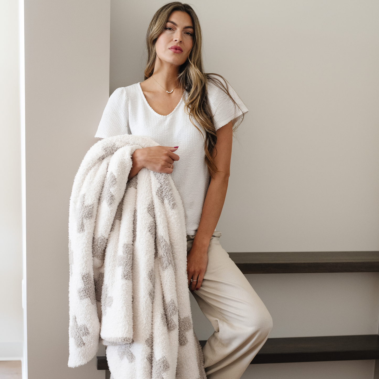 Woman holds soft double layer bamboni swiss cross throw blanket draped over her arm. 