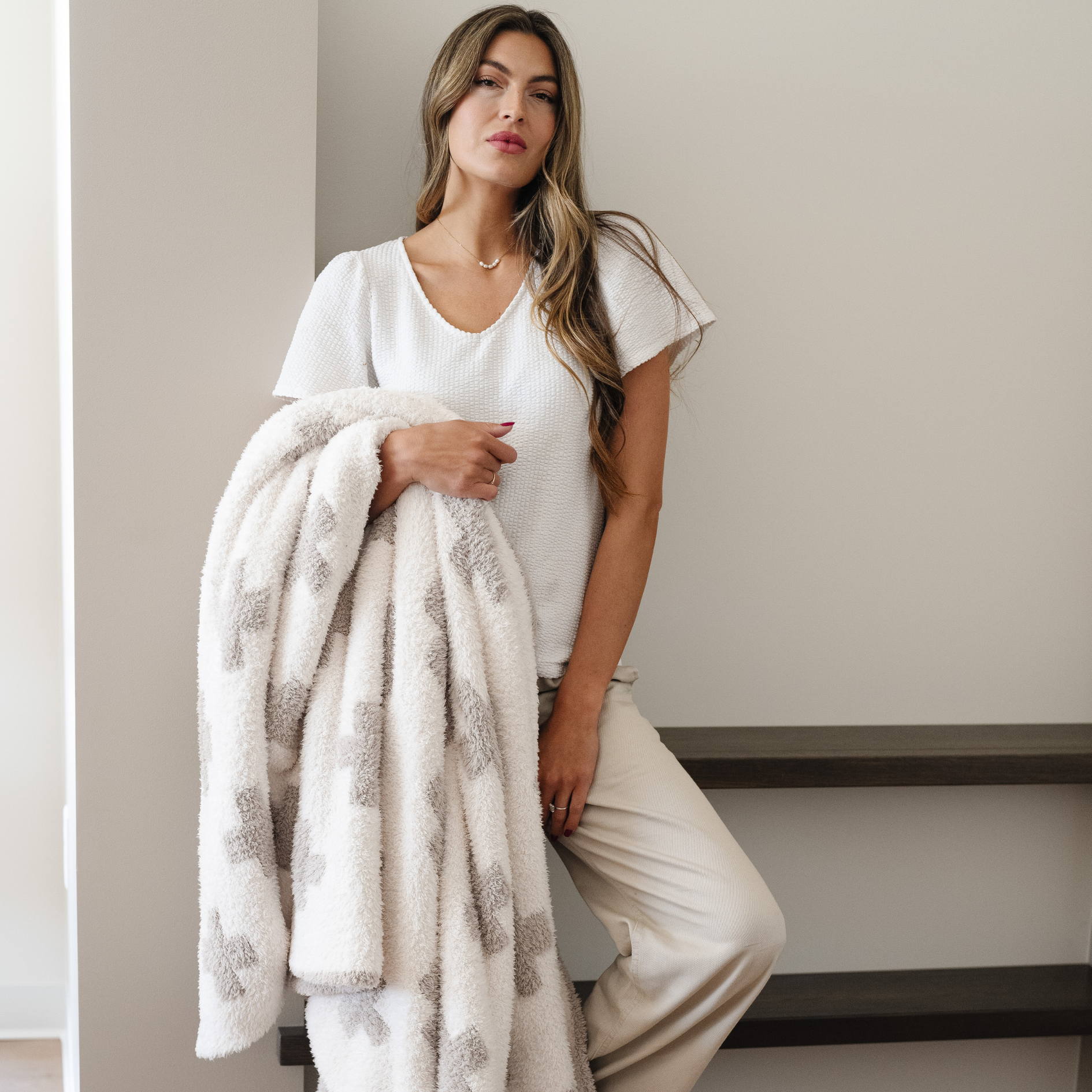 Woman holds soft double layer bamboni swiss cross throw blanket draped over her arm. 