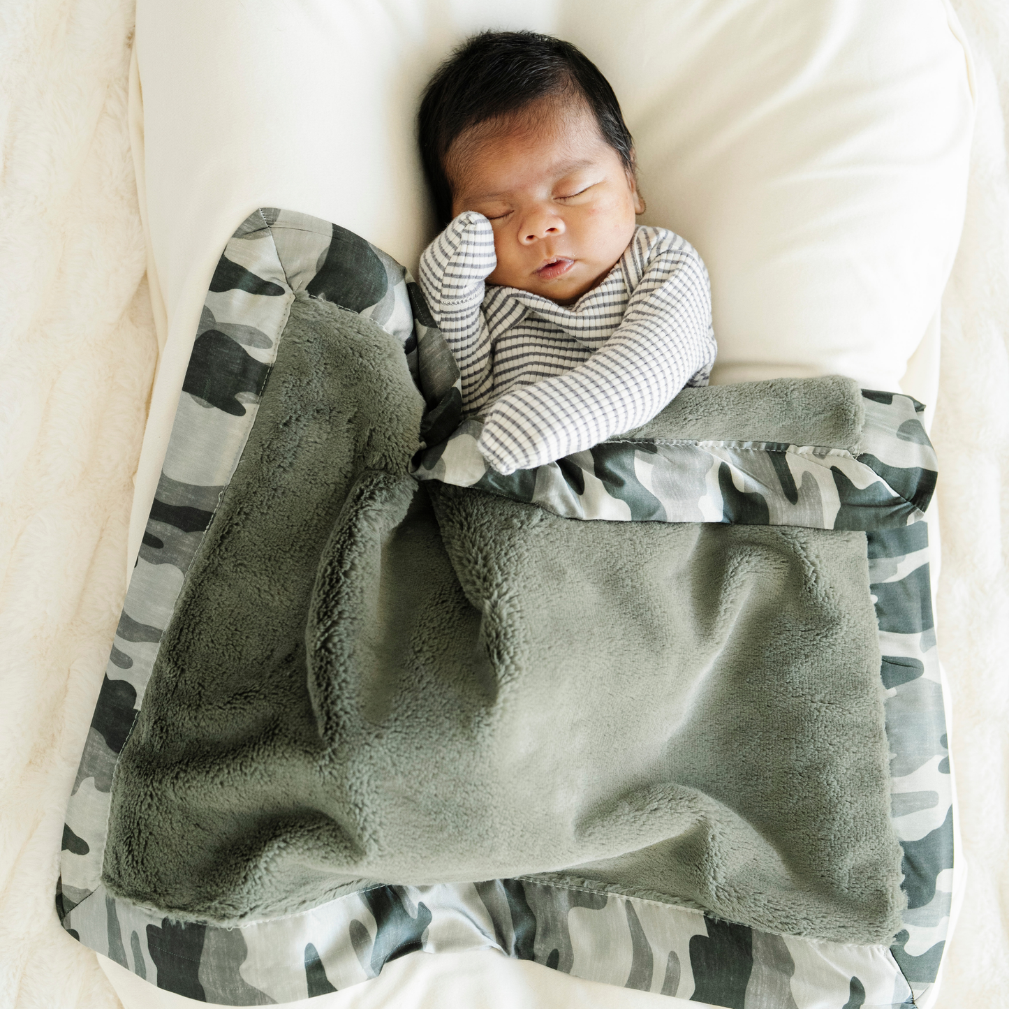Baby boy snuggled with Saranoni Satin Back mini baby blanket in Camo print. 