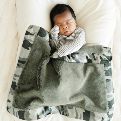 Baby boy snuggled with Saranoni Satin Back mini baby blanket in Camo print. 