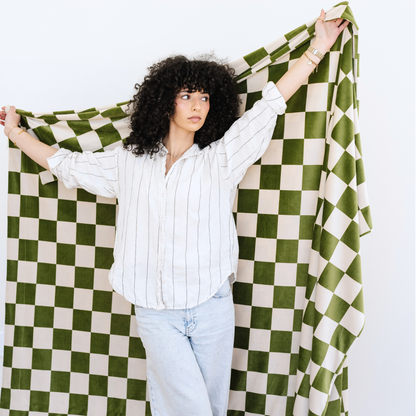 Woman stands with a Minky Stretch olive checkered throw blanket stretched out behind her. 