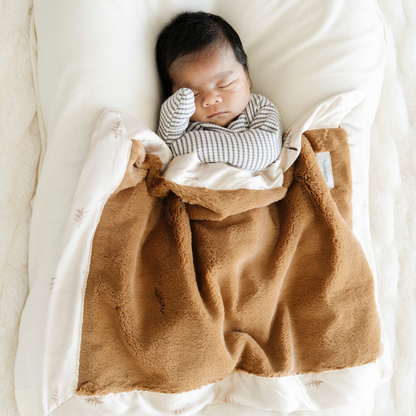 Baby boy snuggled in Saranoni Satin Border mini baby blanket in Cedar print. 