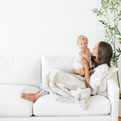 Mom holding baby girl snuggled with a tan faux fur soft receiving baby blanket. 