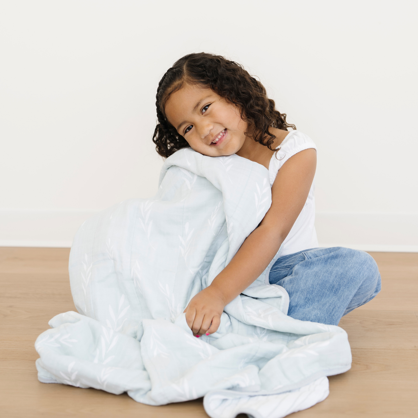 A young girl is snuggled with a Saranoni Cotton Muslin 4-Layer quilt in Olive Branch print. 