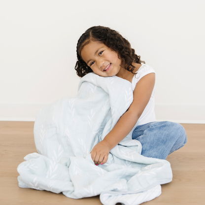 A young girl is snuggled with a Saranoni Cotton Muslin 4-Layer quilt in Olive Branch print. 
