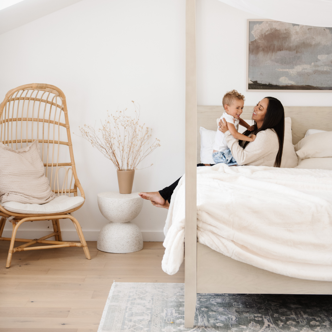 A mother and her son sit on a bed with a Saranoni Grand Faux Fur blanket, featuring an elegant white tone and luxuriously soft texture. This cozy, queen-sized blanket and faux fur blanket offers soothing weight, premium softness, timeless comfort, and is a soft blanket. Perfect as a big blanket and luxury blanket for snuggling or as a luxury bedroom accent, this Saranoni blanket elevates every cozy moment and is a cozy blanket.