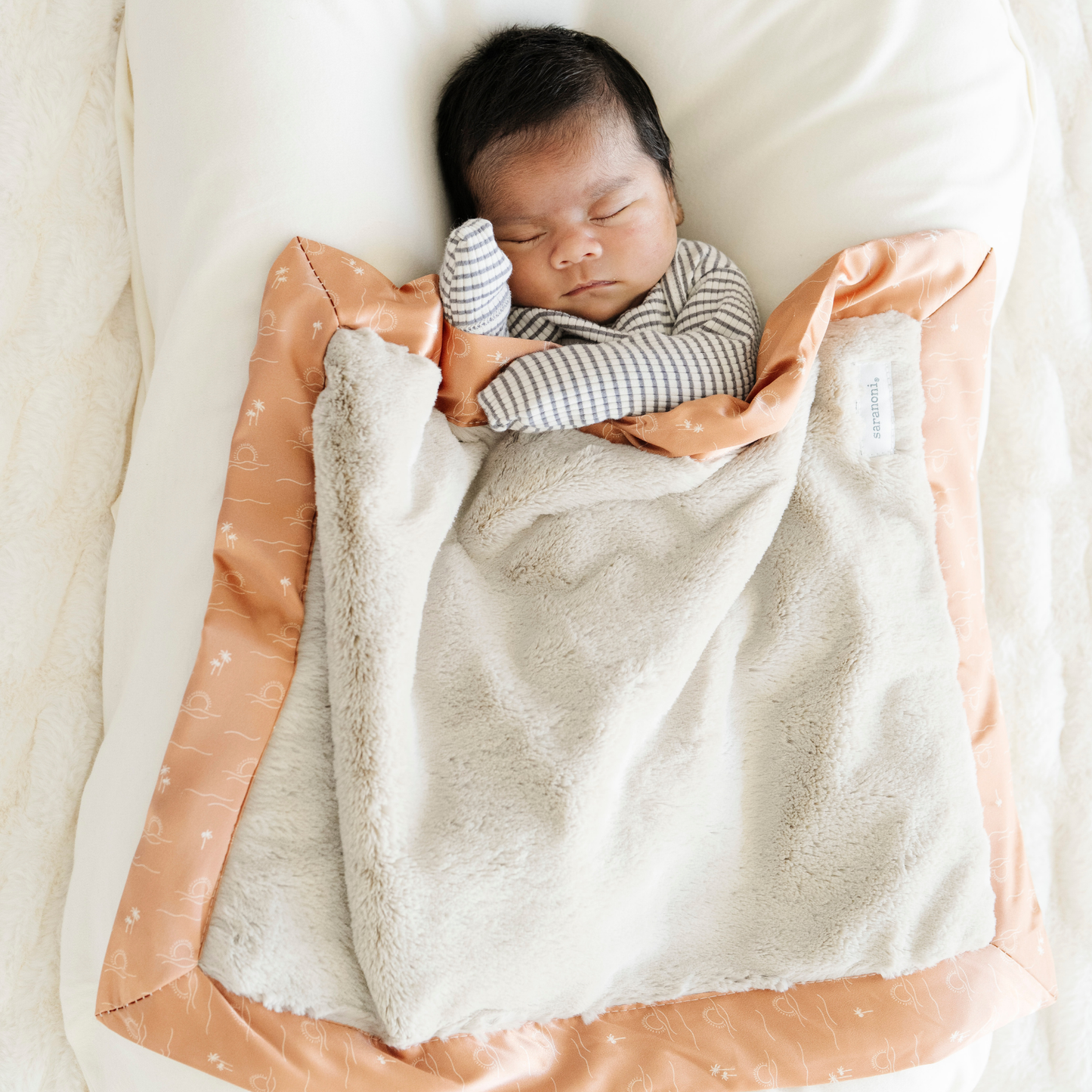 Baby boy snuggled in Saranoni Satin Border Mini baby blanket in Sun & Sea print. 