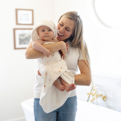 A mother holds her cute baby girl who is wrapped in a Saranoni luxury hooded towel, featuring a soft fabric for quick-drying comfort. This plush baby towel is perfect for bath time, pool time, or beach days, offering a cozy hood and gentle fabric designed for newborns, infants, and toddlers. Adorable gender-neutral baby towel. A must-have baby bath essential, baby shower gift, and new mom must-have. The hooded towel has an ice cream print. The ultimate newborn hooded towel, kids towel, and baby bath towel. 
