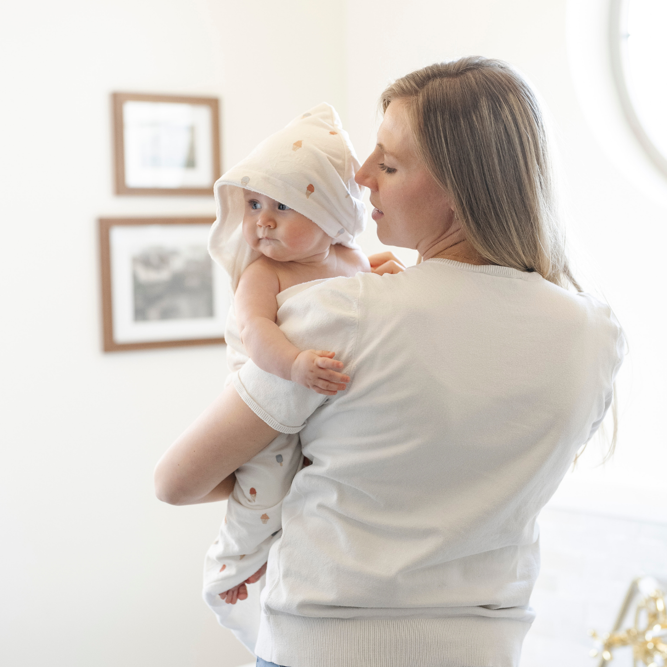 A mother holds her baby girl who is wrapped in a Saranoni luxury hooded towel, featuring a soft fabric for quick-drying comfort. This plush baby towel is perfect for bath time, pool time, or beach days, offering a cozy hood and gentle fabric designed for newborns, infants, and toddlers. Adorable gender-neutral baby towel. A must-have baby bath essential, baby shower gift, and new mom must-have. The hooded towel has an ice cream print. The ultimate newborn hooded towel, kids towel, and baby bath towel. 
