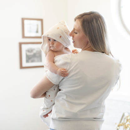 A mother holds her baby girl who is wrapped in a Saranoni luxury hooded towel, featuring a soft fabric for quick-drying comfort. This plush baby towel is perfect for bath time, pool time, or beach days, offering a cozy hood and gentle fabric designed for newborns, infants, and toddlers. Adorable gender-neutral baby towel. A must-have baby bath essential, baby shower gift, and new mom must-have. The hooded towel has an ice cream print. The ultimate newborn hooded towel, kids towel, and baby bath towel. 