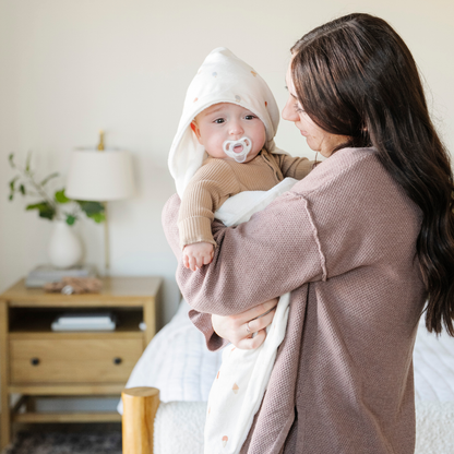 A mother holds her baby boy who has on a Saranoni luxury hooded towel, featuring a soft fabric for quick-drying comfort. This plush baby towel is perfect for bath time, pool time, or beach days, offering a cozy hood and gentle fabric designed for newborns, infants, and toddlers. Adorable gender-neutral baby towel. A must-have baby bath essential, baby shower gift, and new mom must-have. The hooded towel has an ice cream print. The ultimate newborn hooded towel, kids towel, and baby bath towel. 