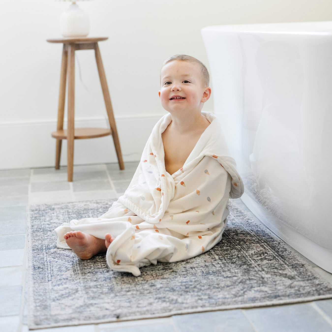 A happy little boy is wrapped in a Saranoni hooded towel. This luxury hooded towel is perfect for bath time, pool days, and beach outings, being gentle on sensitive skin. Designed as a toddler hooded towel, it provides a cozy, plush feel that keeps little ones warm after water play. Ideal for parents looking for the best soft toddler towel that combines style, durability, and ultimate comfort. This kid's towel has an ice cream print. This is a hooded towel for toddlers. 