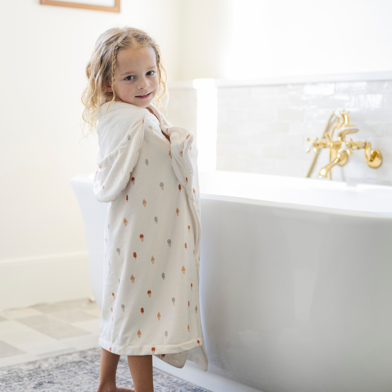 A happy little girl is wrapped in a Saranoni hooded towel. This luxury hooded towel is perfect for bath time, pool days, and beach outings, being gentle on sensitive skin. Designed as a toddler hooded towel, it provides a cozy, plush feel that keeps little ones warm after water play. Ideal for parents looking for the best soft toddler towel that combines style, durability, and ultimate comfort. This kid's towel has an ice cream print. This is a hooded towel for toddlers. 