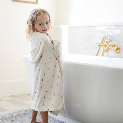 A happy little girl is wrapped in a Saranoni hooded towel. This luxury hooded towel is perfect for bath time, pool days, and beach outings, being gentle on sensitive skin. Designed as a toddler hooded towel, it provides a cozy, plush feel that keeps little ones warm after water play. Ideal for parents looking for the best soft toddler towel that combines style, durability, and ultimate comfort. This kid's towel has an ice cream print. This is a hooded towel for toddlers. 