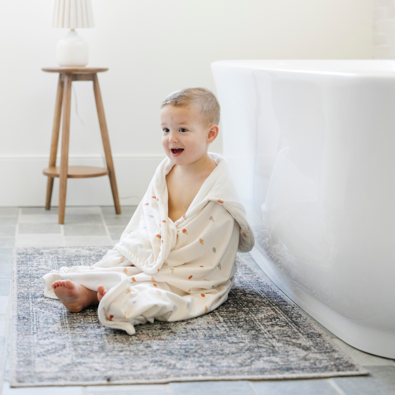 A little boy is wrapped in a Saranoni hooded towel. This luxury hooded towel is perfect for bath time, pool days, and beach outings, being gentle on sensitive skin. Designed as a toddler hooded towel, it provides a cozy, plush feel that keeps little ones warm after water play. Ideal for parents looking for the best soft toddler towel that combines style, durability, and ultimate comfort. This kid's towel has an ice cream print. This is a hooded towel for toddlers and a great bath towel. 