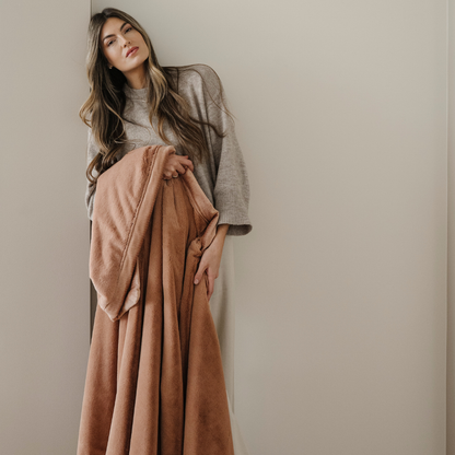 A woman holds a dark peach lush blanket. This soft blanket is a luxury blanket and a Saranoni blanket. This blanket's buttery-soft texture makes it perfect for gifting, relaxing, and using for home decor. Enjoy this cozy blanket for years to come!