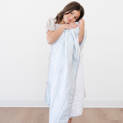 A little girl snuggles a light blue and white blanket that has a floral and striped pattern. This Saranoni blanket is a cotton muslin blanket. This is a great baby blanket or toddler blanket and is oh-so soft. 
