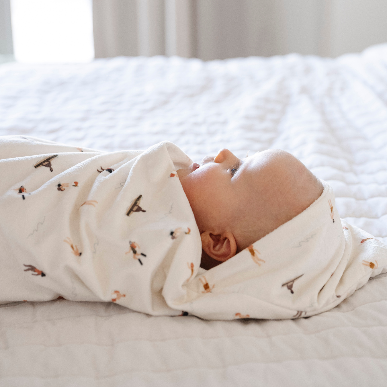 A baby girl is wrapped in a Saranoni luxury hooded towel, featuring a soft fabric for quick-drying comfort. This plush baby towel is perfect for bath time, pool time, or beach days, offering a cozy hood and gentle fabric designed for newborns, infants, and toddlers. Adorable gender-neutral baby towel. A must-have baby bath essential, baby shower gift, and new mom must-have. The hooded towel has a print with people on it. The ultimate newborn hooded towel, kids towel, newborn towel, and baby bath towel. 