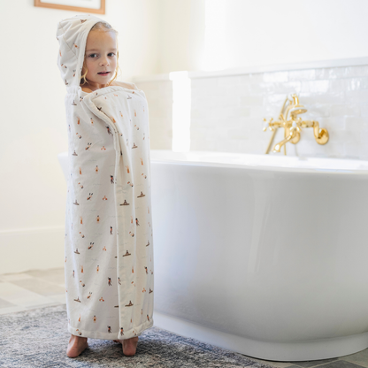 A little girl is wrapped in a Saranoni hooded towel. This luxury hooded towel is perfect for bath time, pool days, and beach outings, offering quick-drying warmth while being gentle on sensitive skin. Designed as a toddler hooded towel, it provides a cozy, plush feel that keeps little ones warm after water play. Ideal for parents looking for the best soft toddler towel that combines style, durability, and ultimate comfort. This kid's towel has a print with people on it. This is a hooded towel for toddlers. 