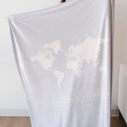 Person holding a glacier blue LDS missionary blanket featuring a world map design and the words "Called to Serve," meaningful missionary gift blanket celebrating faith, service, and missionary journeys around the world.