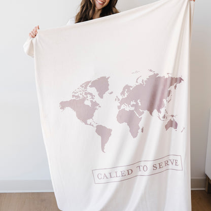 Woman holding a shell cream LDS missionary blanket featuring a world map design and the words "Called to Serve," meaningful missionary gift blanket celebrating faith, service, and missionary journeys around the world.