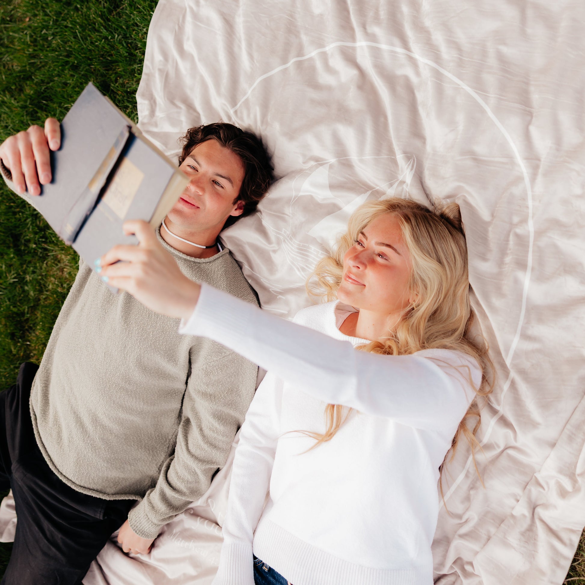 Man and woman relaxing on a cobblestone Fishers of Men Christian blanket while reading outdoors on the grass