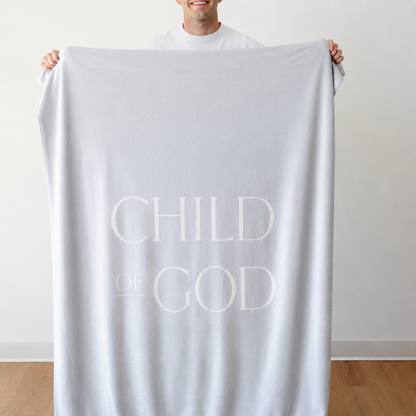 Person holding a light glacier blue Christian blanket featuring the words "Child of God," soft faith-inspired throw blanket displayed against a neutral indoor background.