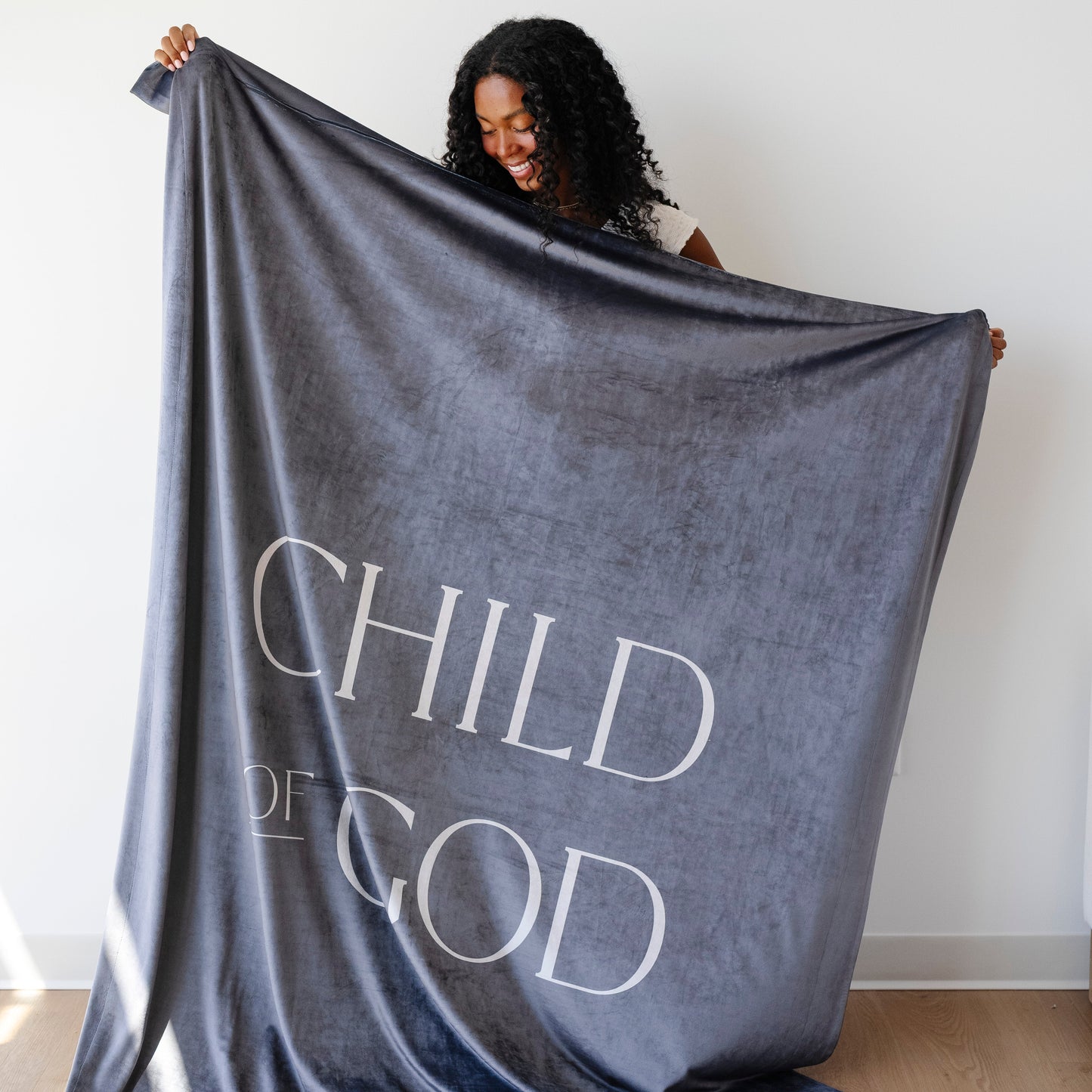 Person holding a dark obsidian Christian blanket featuring the words "Child of God," soft faith-inspired throw blanket displayed against a neutral background.