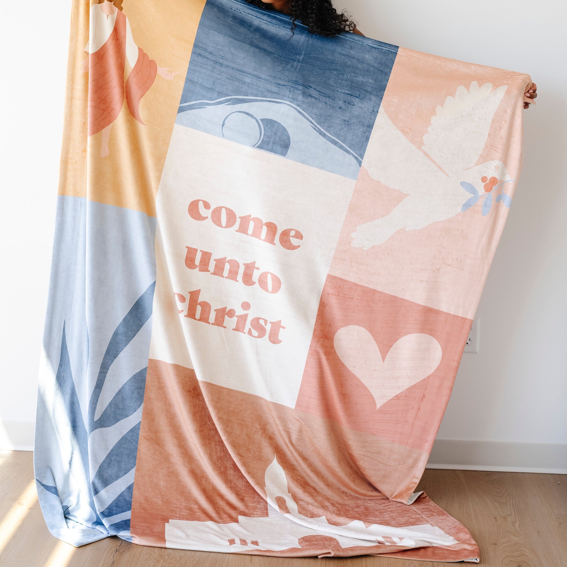 Person holding a Come Unto Christ LDS blanket featuring pastel faith-centered artwork, a dove, heart, and the words "Come Unto Christ," meaningful blanket for LDS youth, girls camp, youth conference, and Christian homes.
