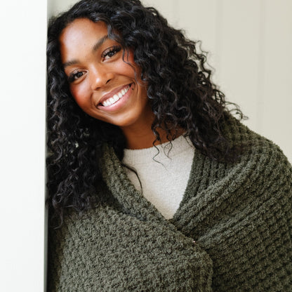 Detailed shot of a woman wrapped up in the warmth of a green waffle knit blanket.