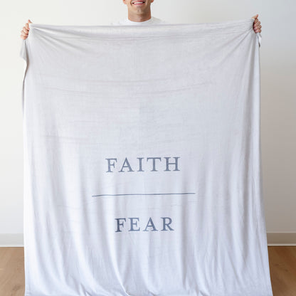 Person holding a gray Christian blanket featuring the words "Faith Over Fear," faith-inspired throw blanket offering comfort, encouragement, and a reminder to trust God through life's challenges.
