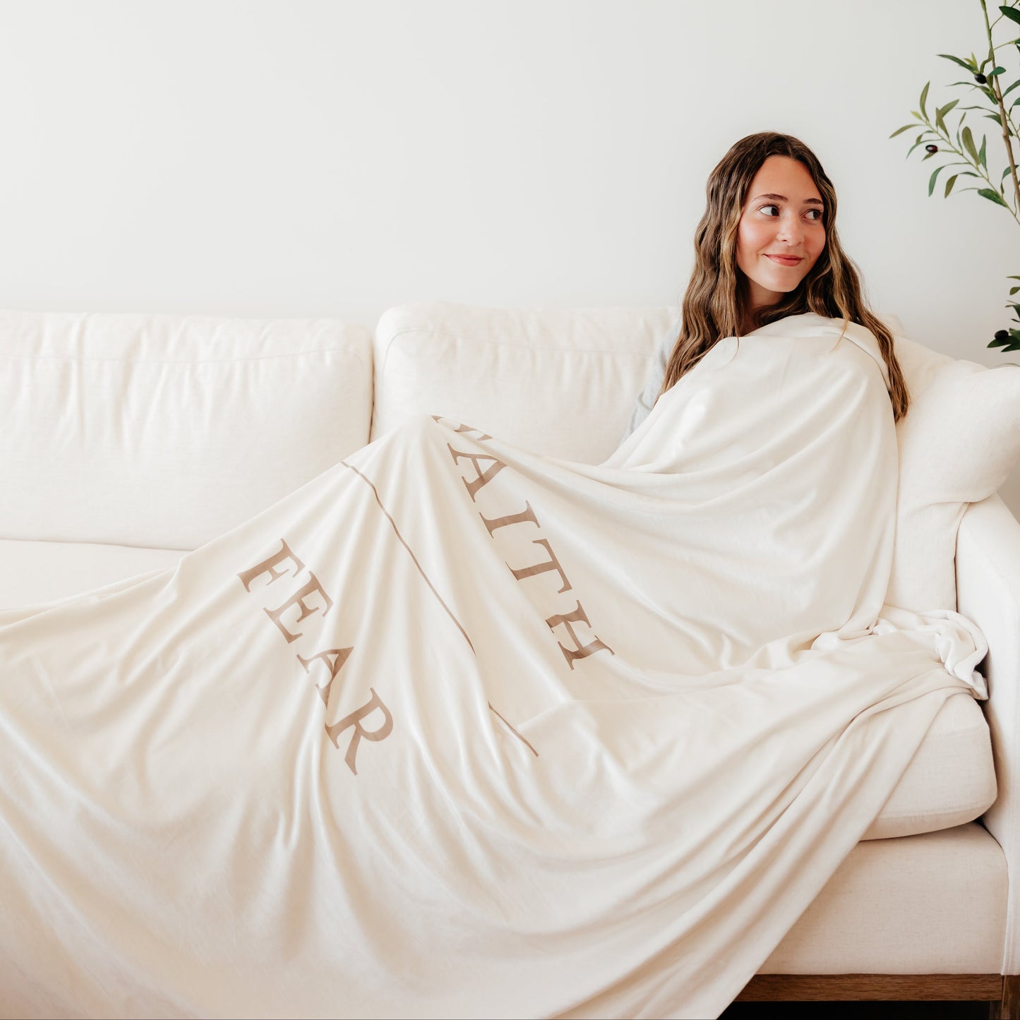 Woman wrapped in a shell cream Christian blanket featuring the words "Faith Over Fear," soft faith-inspired throw blanket offering comfort, encouragement, and a reminder to trust in God through life's challenges.