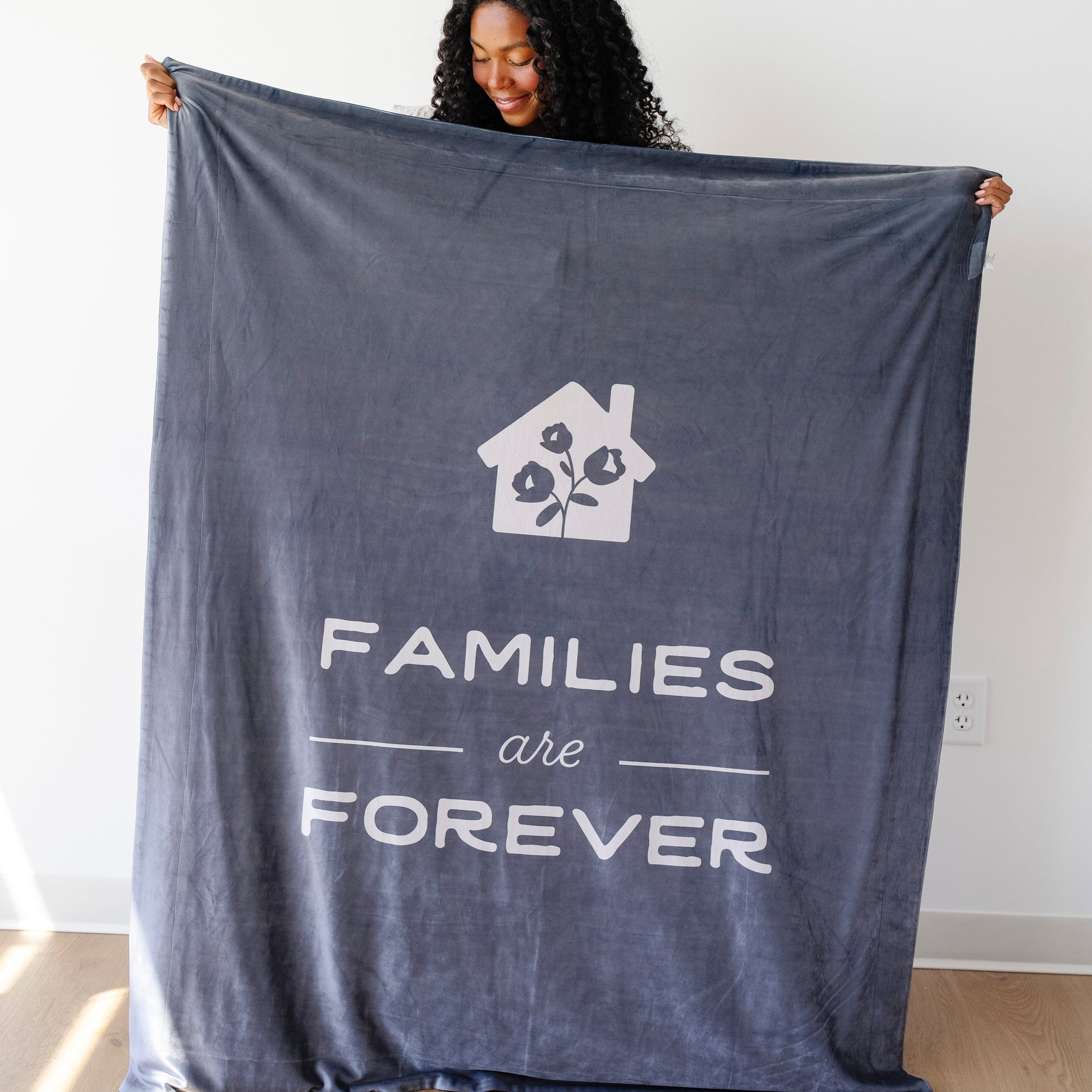 Person holding a dark obsidian LDS blanket featuring the words "Families Are Forever" and a home design, soft faith-inspired throw blanket celebrating eternal families.
