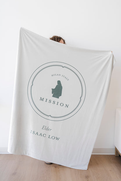 Person holding a soft sage green personalized missionary blanket featuring custom missionary details and mission-inspired artwork.