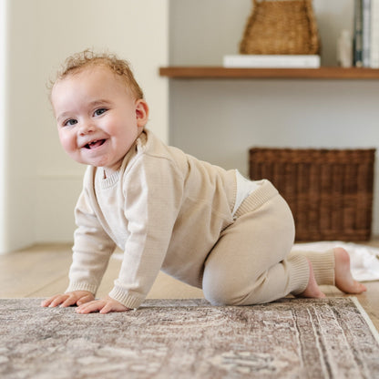 A baby boy crawls on a wooden floor. He is wearing a light tan, 100% cotton baby outfit that combines style and comfort. The Saranoni cloud-soft cotton set features a breathable waistband, loosely fitted sleeves, and elevated button details, making it perfect for everyday wear or special occasions. This heirloom-quality baby clothing offers timeless style and ultimate comfort. Ideal for parents searching for luxury baby clothes, soft cotton baby sets, or high-quality infant outfit.