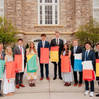 Group of missionaries standing outside a templeholding personalized mission flag blankets, custom LDS missionary keepsake blankets for mission farewells and homecomings.