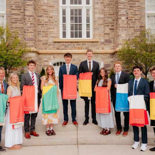 Group of missionaries standing outside a templeholding personalized mission flag blankets, custom LDS missionary keepsake blankets for mission farewells and homecomings.