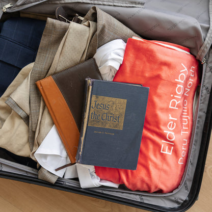 Open suitcase packed for missionary service with a personalized mission flag blanket and scriptures, custom LDS missionary keepsake blanket for mission preparation, travel, and meaningful gifts.