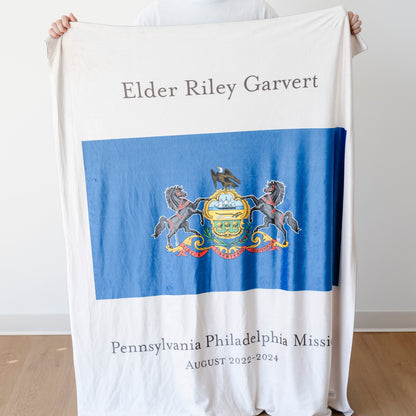 Person holding a personalized missionary blanket featuring the Pennsylvania Philadelphia Mission flag, missionary name, and custom mission dates.