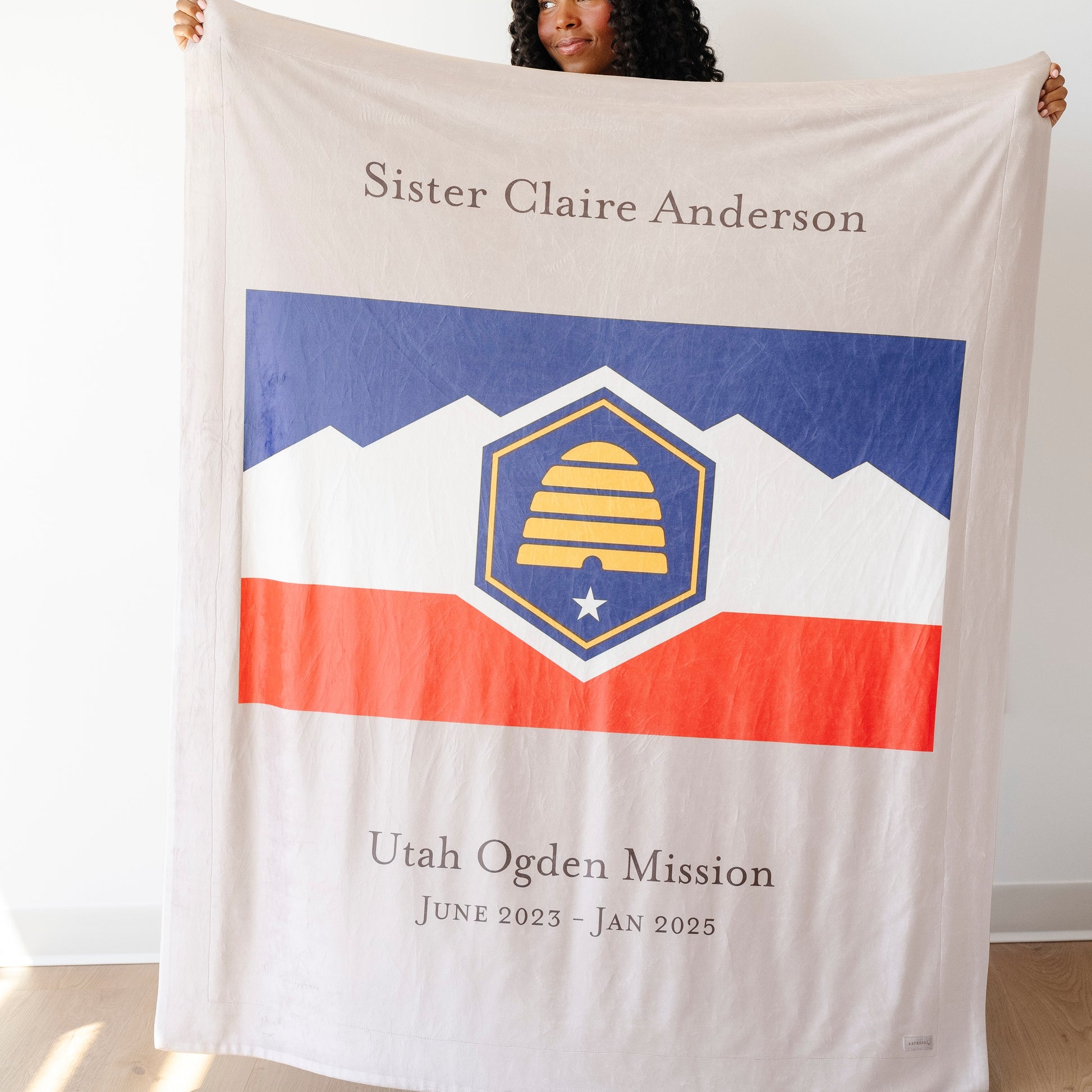 Person holding a personalized missionary blanket featuring a custom mission flag, missionary name, and service dates, meaningful LDS missionary gift for mission farewells, homecomings, and missionary families.