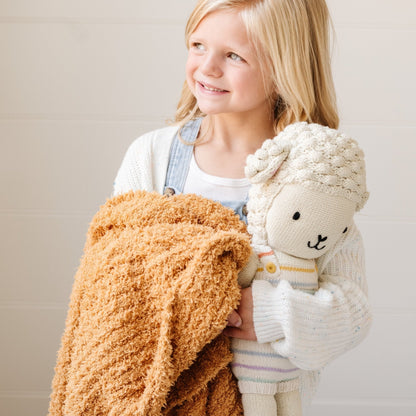Smiling little girl holding stuffed lamb and extra soft Golden RIBBED BAMBONI TODDLER BLANKETS - Saranoni