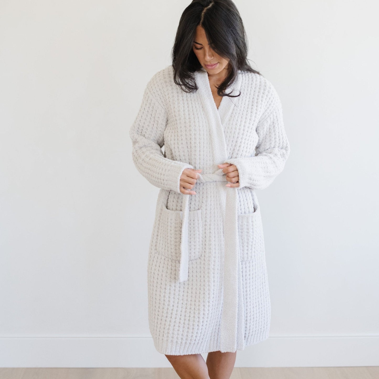 Woman in a light gray waffle knit robe, standing in a bright room.