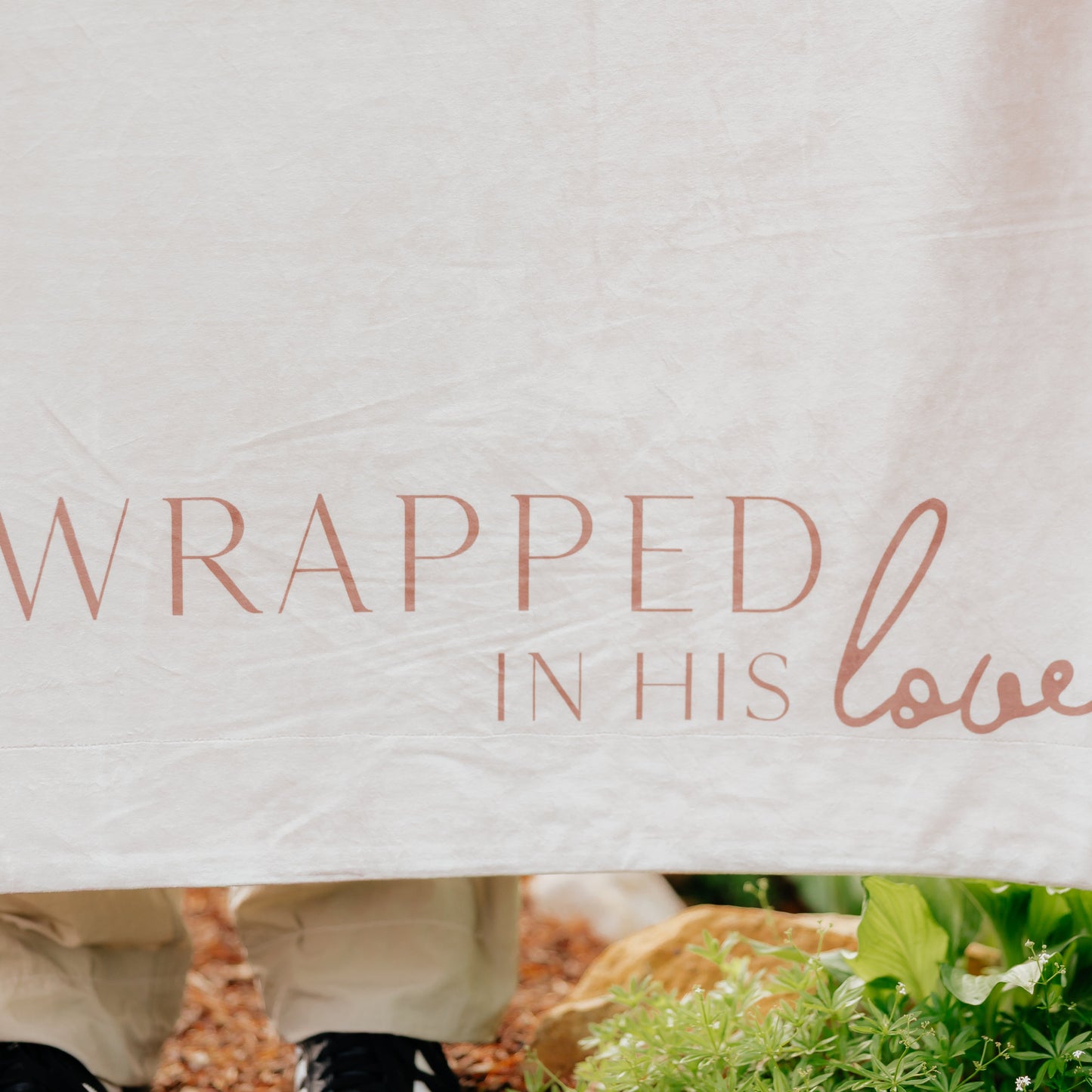 Close-up of a cream Christian blanket featuring the words "Wrapped in His Love" in elegant script lettering.